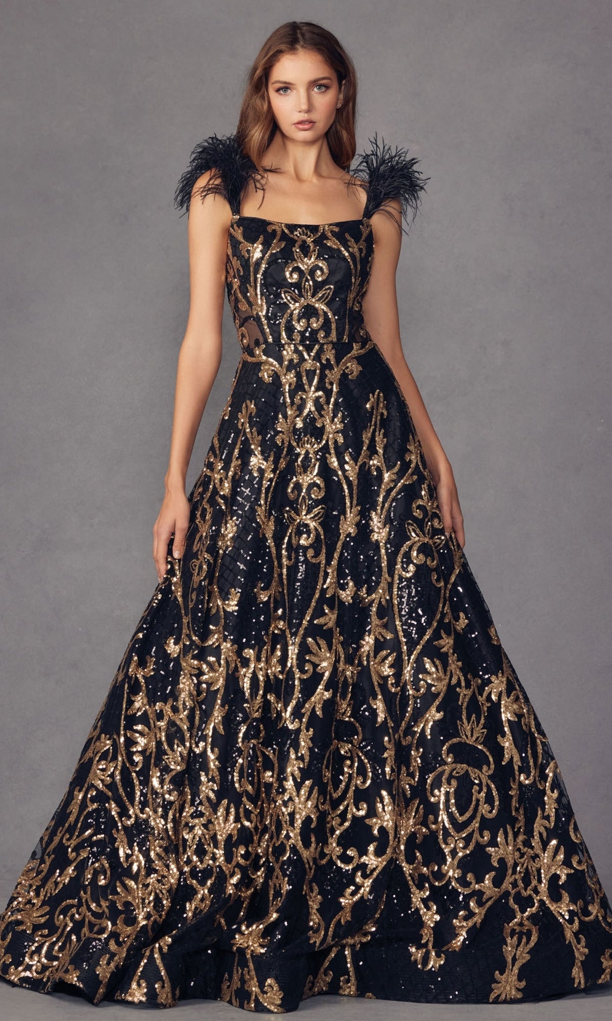 A woman models the Feathered-Cap-Sleeve Long Sequin Prom Ball Gown 297—an elegant black evening gown with gold sequin embroidery and feathered cap sleeves—while standing against a plain gray background.